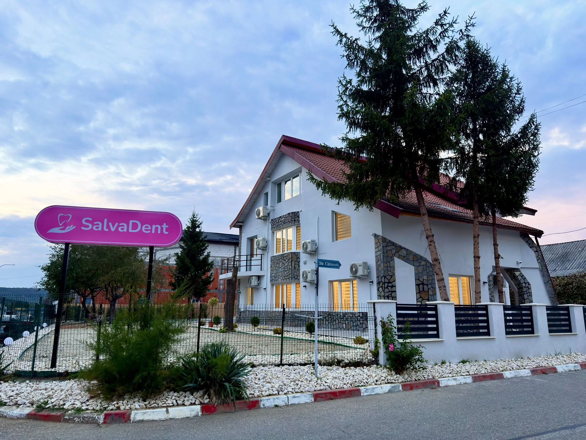 Clădirea clinicii seara, cu ferestrele luminate și firma SalvaDent